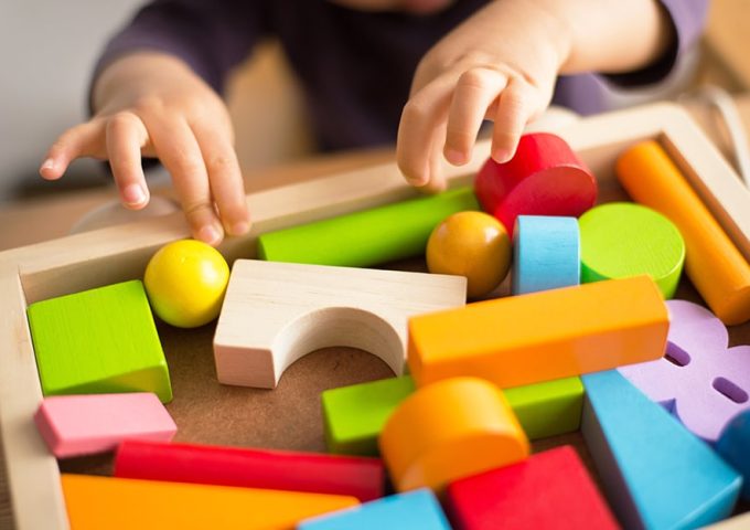 Delle mani di un bambino dell'asilo nido stanno per prendere delle colorate costruzioni in legno da una cassetta