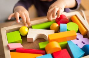Delle mani di un bambino dell'asilo nido stanno per prendere delle colorate costruzioni in legno da una cassetta
