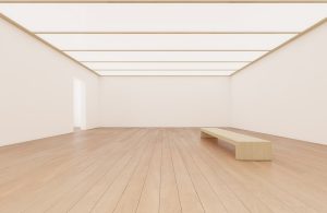 Una sala di museo completamente vuota, con panca in legno, pavimento a parquet, soffitto luminoso a pannelli, pareti bianche e porta