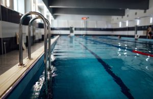 Una grandi piscina pubblica vista da una prospettiva poco superiore al livello dell'acqua, con la scaletta in primo piano