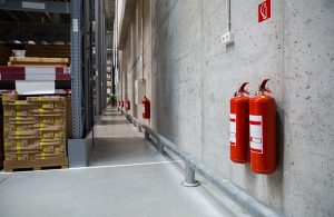 Interno di un magazzino industriale con due estintori antincendio appesi al muro, in primo piano