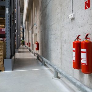 Interno di un magazzino industriale con due estintori antincendio appesi al muro, in primo piano