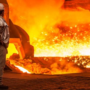 Operaio di un altoforno con tuta in amianto guarda un impianto di produzione di ghisa con scintille e altissime temperature