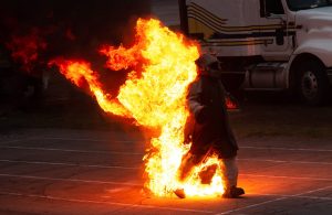 Un uomo cammina tra le fiamme equipaggiato da abiti in tessuti ignifughi