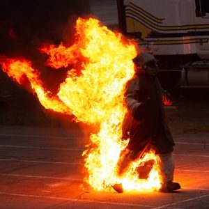Un uomo cammina tra le fiamme equipaggiato da abiti in tessuti ignifughi