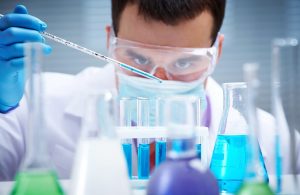 Tecnico di laboratorio con occhialini protettivi e guanti maneggia provette con un liquido azzurro all'interno