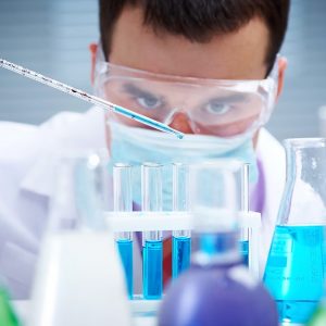 Tecnico di laboratorio con occhialini protettivi e guanti maneggia provette con un liquido azzurro all'interno