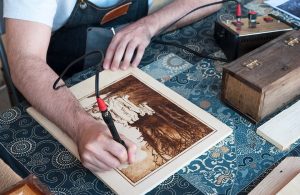Un artista mentre incide il legno con una macchinetta elettrica per la pirografia