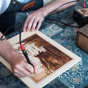 Un artista mentre incide il legno con una macchinetta elettrica per la pirografia