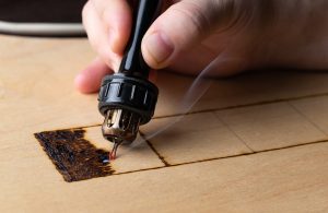 Primo piano della mano di un artista che incide il legno con una macchinetta elettrica per la tipografia