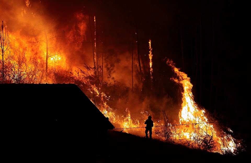 Scena notturna di un incendio boschivo. Si vede la sagoma di un vigile del fuoco davanti alle fiamme