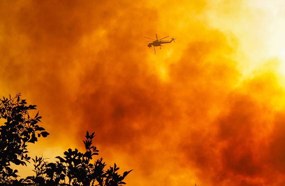 Elicottero in volo durante un incendio. Il cielo è interamente pieno di fumo e colorato d'arancione
