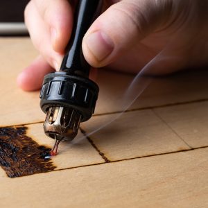 Primo piano della mano di un artista che incide il legno con una macchinetta elettrica per la tipografia