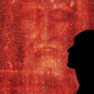 Silhouette di un ragazzo di profilo con sullo sfondo il primo piano sul volto della Sindone di Torino dai colori virati in rosso