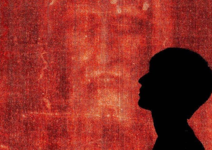 Silhouette di un ragazzo di profilo con sullo sfondo il primo piano sul volto della Sindone di Torino dai colori virati in rosso