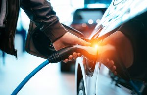 Fare il pieno a un'auto elettrica, si vede una mano che tiene lo spinotto agganciato al serbatoio di un'auto