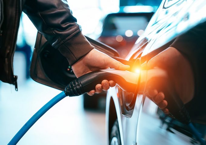 Fare il pieno a un'auto elettrica, si vede una mano che tiene lo spinotto agganciato al serbatoio di un'auto