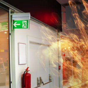 Incendio all'interno di un ufficio in cui si vedono il cartello dell'uscita di sicurezza, un estintore e una porta