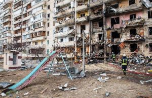 Scenario di guerra a Kyev, in Ucraina, con un'area dei giochi per bambini distrutta davanti a un palazzo colpito dai missili, con due pompieri che passano tra le macerie