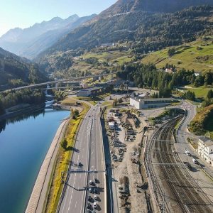 Visuale panoramica dall'alto dell'ingresso al tunnel autostradale e ferroviario del San Gottardo, immerso tra le montagne e parallelo al fiume