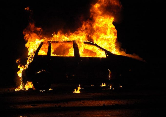 Silhouette di un'auto in fiamme, di notte, vista di lato