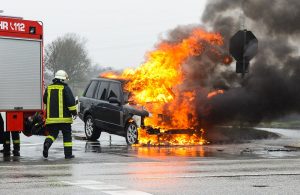 Un pompiere interviene in un incendio di un'auto su strada che è in fiamme dopo un incidente