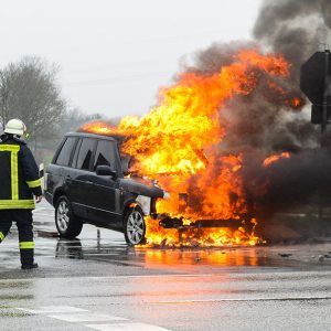 Un pompiere interviene in un incendio di un'auto su strada che è in fiamme dopo un incidente