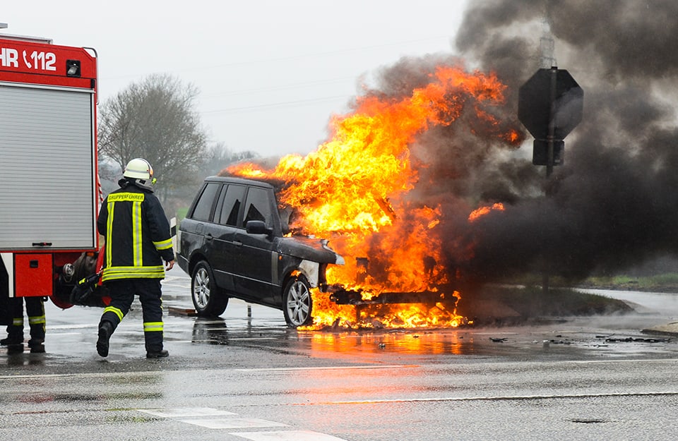 Un pompiere interviene in un incendio di un'auto su strada che è in fiamme dopo un incidente