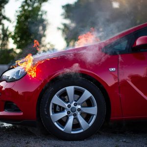 La parte frontale di un'auto rossa, vista di lato, con fiamme che escono dal cofano