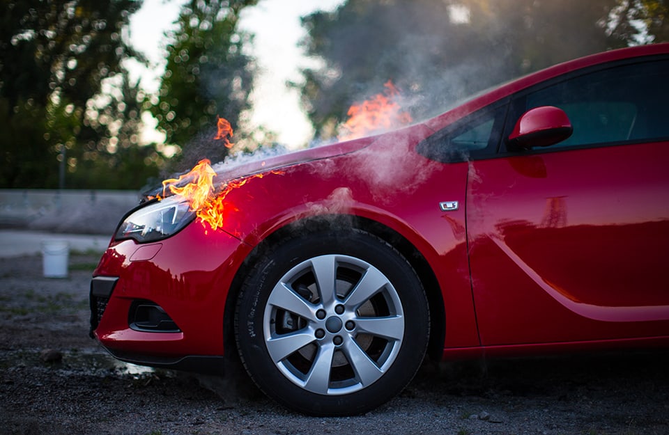 La parte frontale di un'auto rossa, vista di lato, con fiamme che escono dal cofano