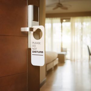 Porta tagliafuoco in legno di un hotel: si intravede la camera d'albergo e c'è il cartello “non disturbare” appeso alla maniglia