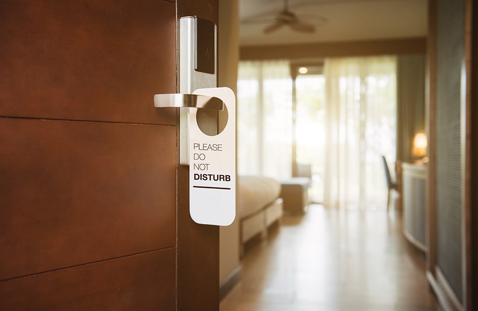 Porta tagliafuoco in legno di un hotel: si intravede la camera d'albergo e c'è il cartello “non disturbare” appeso alla maniglia