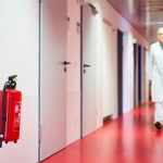 Un medico cammina lungo una corsia d'ospedale e in primo piano si vede un estintore rosso