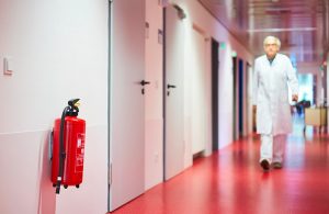 Un medico cammina lungo una corsia d'ospedale e in primo piano si vede un estintore rosso