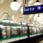 Una stazione della metropolitana di Parigi con un treno che sta passando e in primo piano un cartello luminoso che indica l'uscita