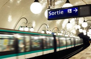 Una stazione della metropolitana di Parigi con un treno che sta passando e in primo piano un cartello luminoso che indica l'uscita