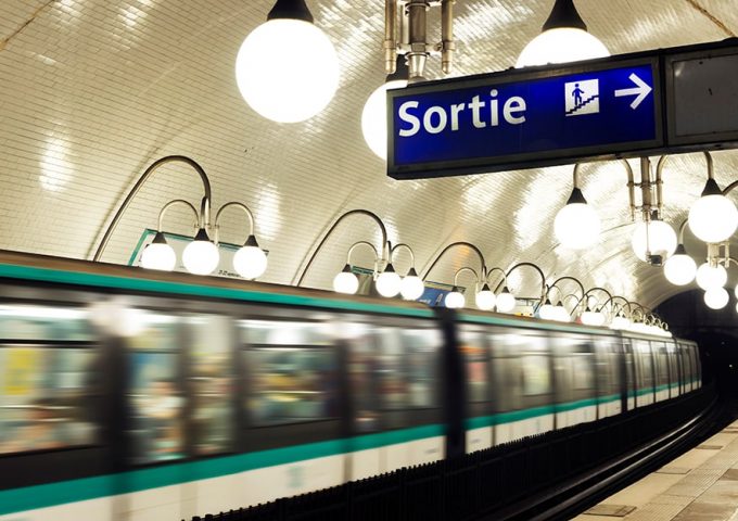 Una stazione della metropolitana di Parigi con un treno che sta passando e in primo piano un cartello luminoso che indica l'uscita