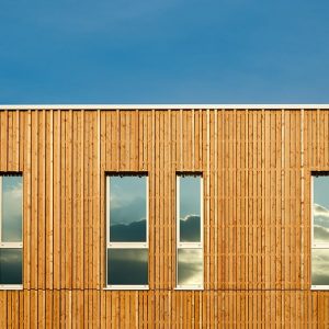 Struttura architettonica in legno con diverse finestre in verticale, sulle quali si riflette il panorama di fronte