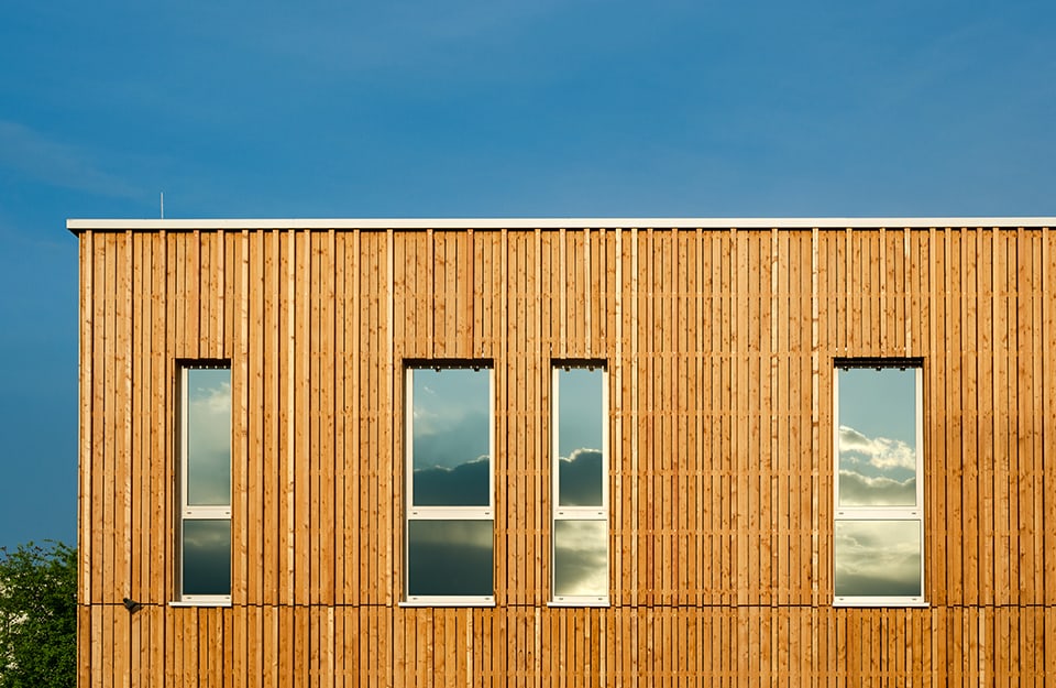 Struttura architettonica in legno con diverse finestre in verticale, sulle quali si riflette il panorama di fronte
