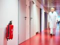 Un medico cammina lungo una corsia d'ospedale e in primo piano si vede un estintore rosso