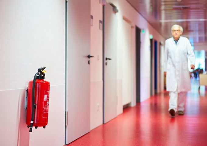 Un medico cammina lungo una corsia d'ospedale e in primo piano si vede un estintore rosso