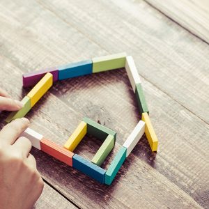 Due mani stanno costruendo con dei mattoncini in legno colorati la forma stilizzata di una casa