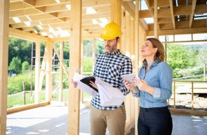 Una donna visita il cantiere di una casa in legno e il capocantiere con casco giallo studia le piante del progetto