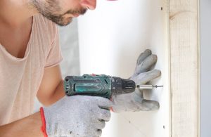 Un operaio sta fissando con il trapano e delle viti una lastra di cartongesso alla parete