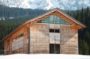 Grande edificio in legno e vetro, costruito seguendo i principi della bioedilizia vicino a un bosco in mezzo alle montagne