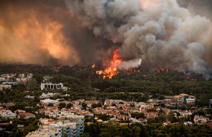 Vista dall'alto dei sobborghi di Atene, in Grecia, durante un incendio scoppiato nell'agosto del 2021. Un elicottero dei pompieri è in volo tra fumo e fiamme