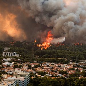 Vista dall'alto dei sobborghi di Atene, in Grecia, durante un incendio scoppiato nell'agosto del 2021. Un elicottero dei pompieri è in volo tra fumo e fiamme