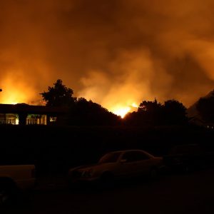 Silhouette di un'abitazione a ridosso di un incendio che sta interessando le colline retrostanti