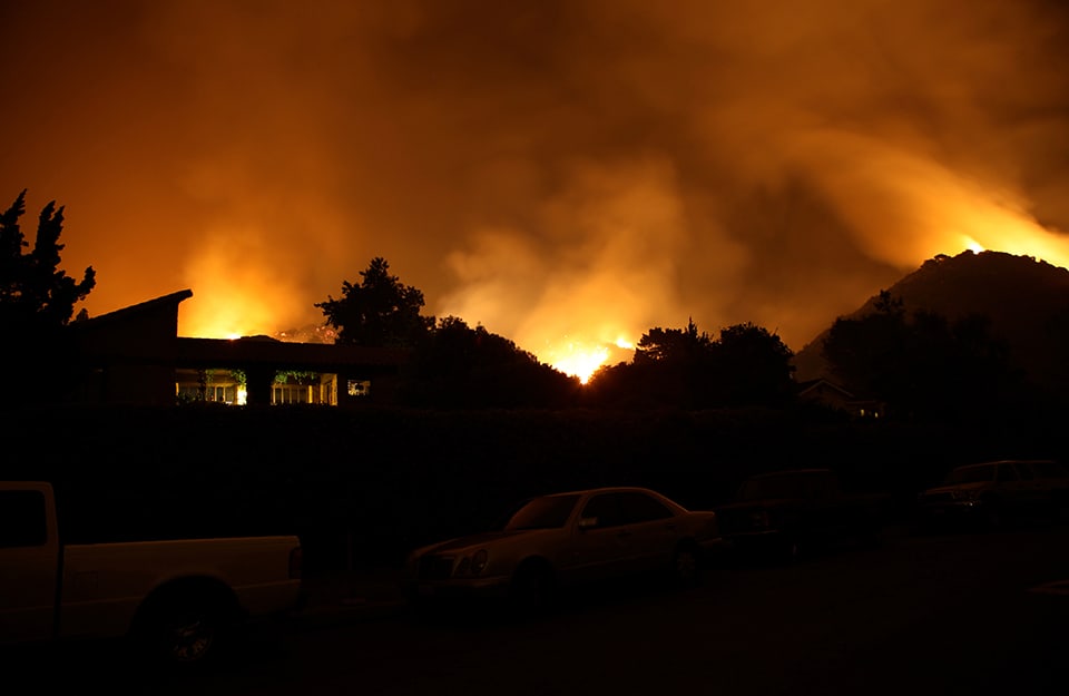 Silhouette di un'abitazione a ridosso di un incendio che sta interessando le colline retrostanti
