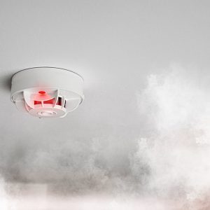 Un rilevatori di fumi antincendio in azione in mezzo a una nuvola di fumo bianco in una stanza con soffitto chiaro